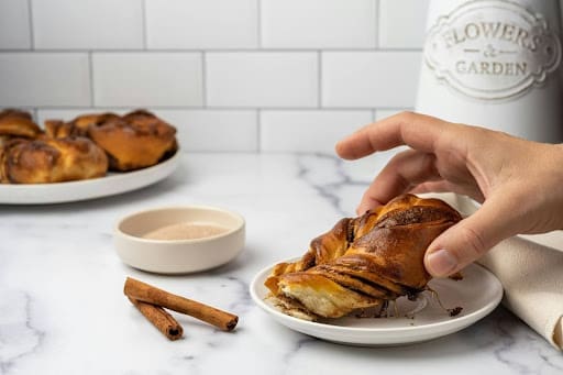 Hand reaching for a cinnamon pastry on a plate, highlighting the concept of honoring cravings and choice—central to answering what is intuitive eating.