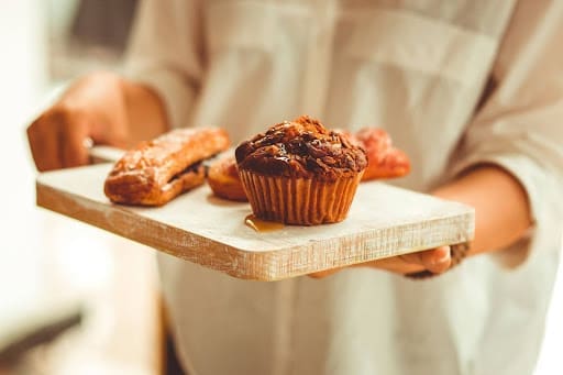 Person holding a wooden tray with pastries and a muffin, symbolizing food freedom and choice—key concepts in answering the question: what is intuitive eating?