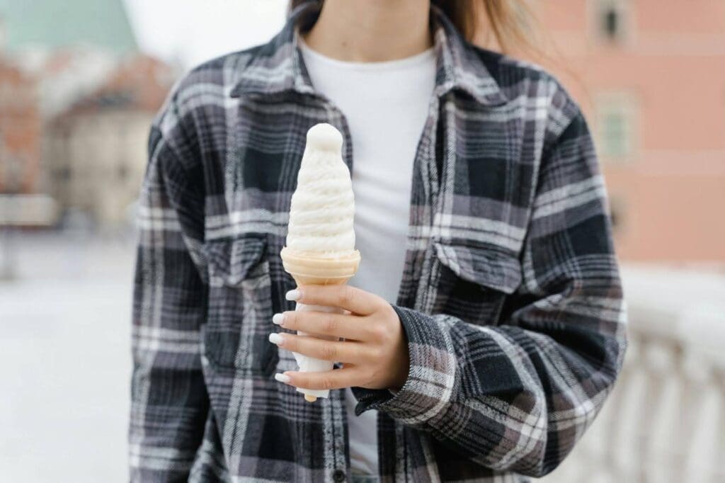 Woman in a plaid shirt holding a soft-serve ice cream cone outdoors, symbolizing emotional hunger vs physical hunger and the subtle signs of emotional eating
