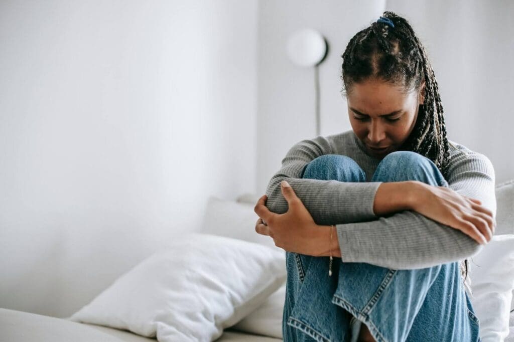 Woman sitting with arms wrapped around knees, representing emotional distress and the mental health impact of disordered eating and food anxiety.