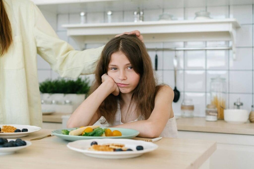 Young picky eater sitting at the table refusing food, illustrating common picky eating challenges and how to help a picky eater