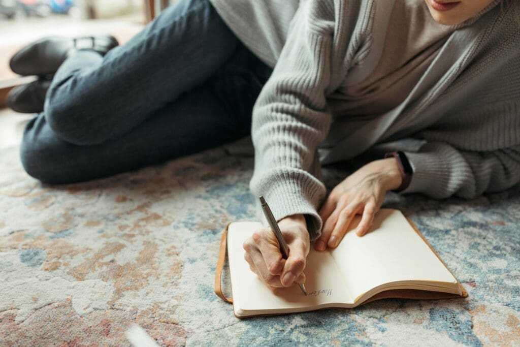 Person sitting on a rug writing in a journal, reflecting on their relationship with food and disordered eating recovery