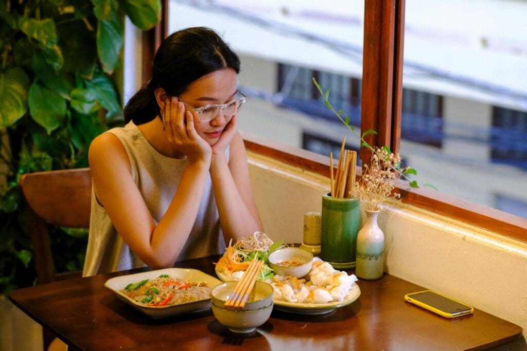 Woman sitting at a restaurant table looking hesitantly at her meal, reflecting the stress of anxiety and food in social settings.