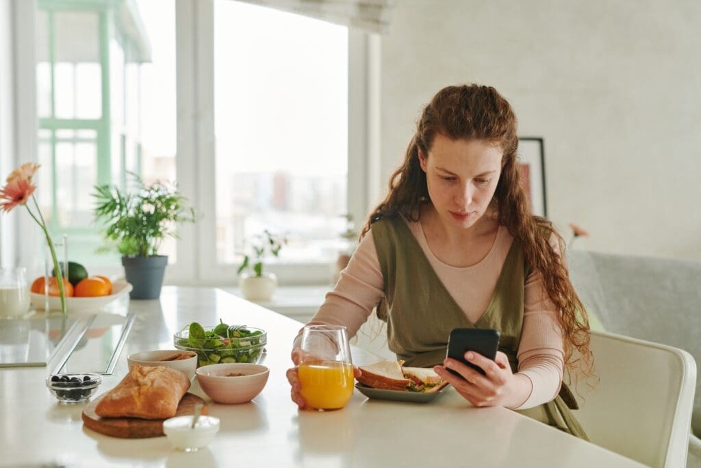 Woman distracted by her phone while eating, disconnected from her meal